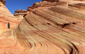 Person hiking along the dramatic curved sandstone formations in The Wave, Arizona.