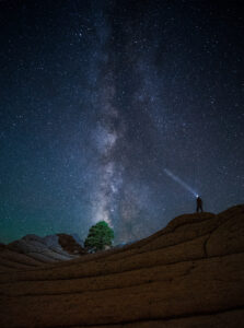 Kanab Tour Company guide poses for a photo. He stands under the Milky Way at White Pocket. his headlamp shining into the stars.